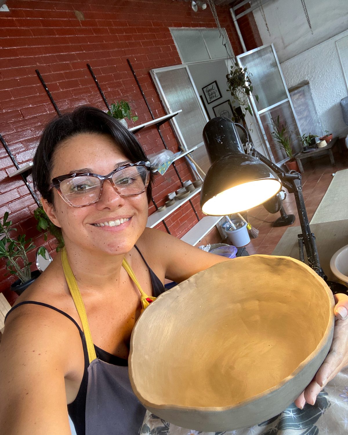 Maria Fernanda Azevedo no ateliê da Olaria Cajuti, de avental, segurando uma tigela crua