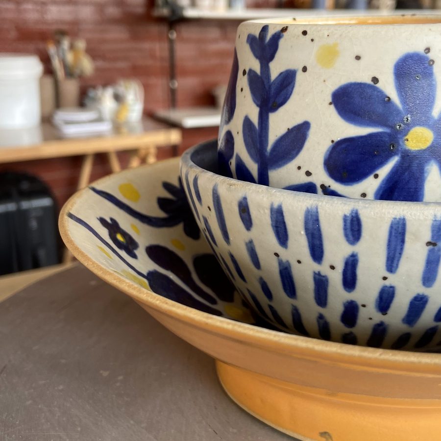 Tigelas pintadas à mão com flores azuis, empilhadas sobre um prato amarelo
